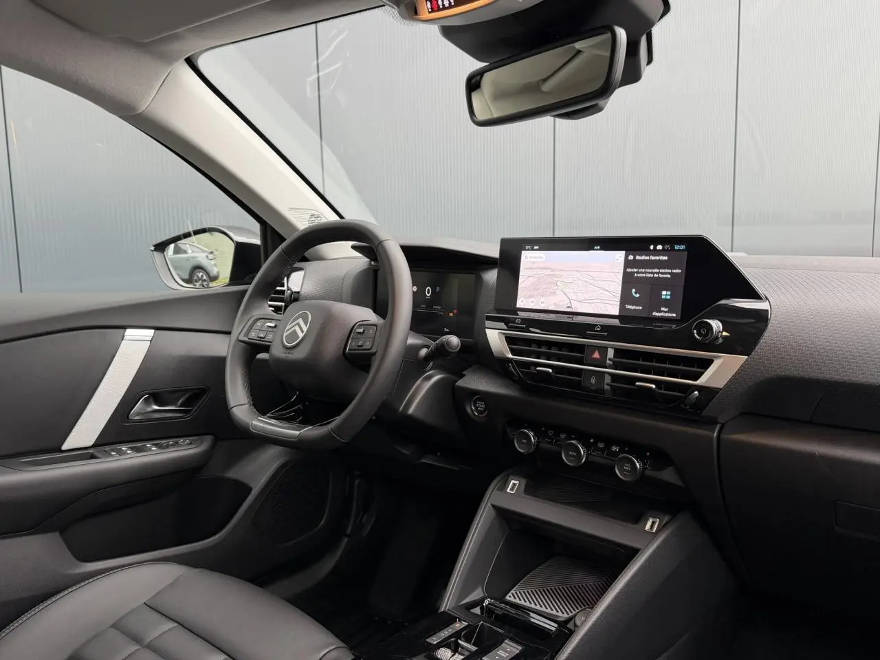 Vue intérieure côté conducteur de la Citroën C4 2025, tableau de bord noir avec écran tactile et volant cuir.