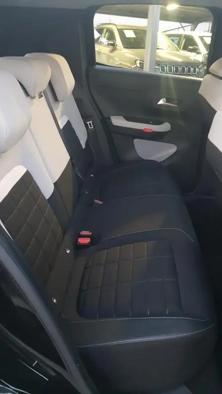 Vue intérieure arrière côté droit de la Citroën C3 2025 noire, sièges bicolores noir et blanc avec surpiqûres visibles.