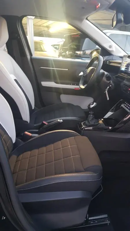 Intérieur avant droit de la Citroën C3 2025 noire, sièges bi-ton, volant réglable et levier de boîte manuelle visible.