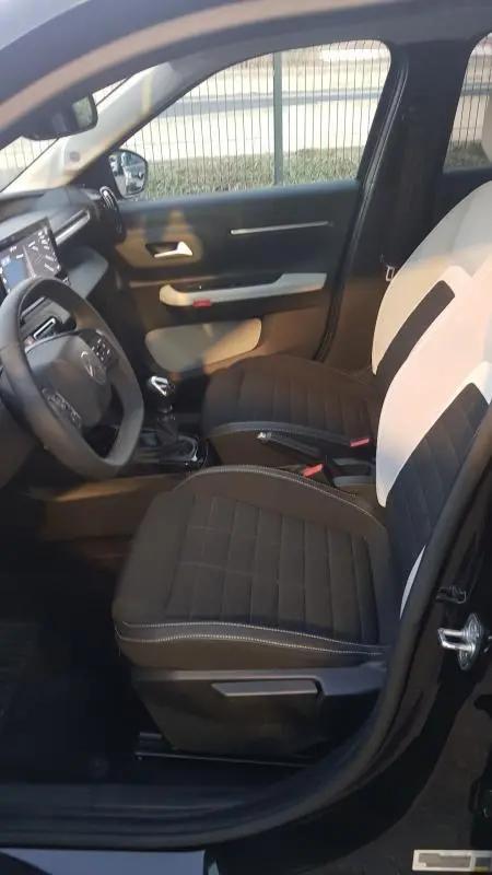 Vue intérieure côté conducteur de la Citroën C3 noire 2025, sièges bicolores noirs et blancs, volant multifonction et boîte manuelle.