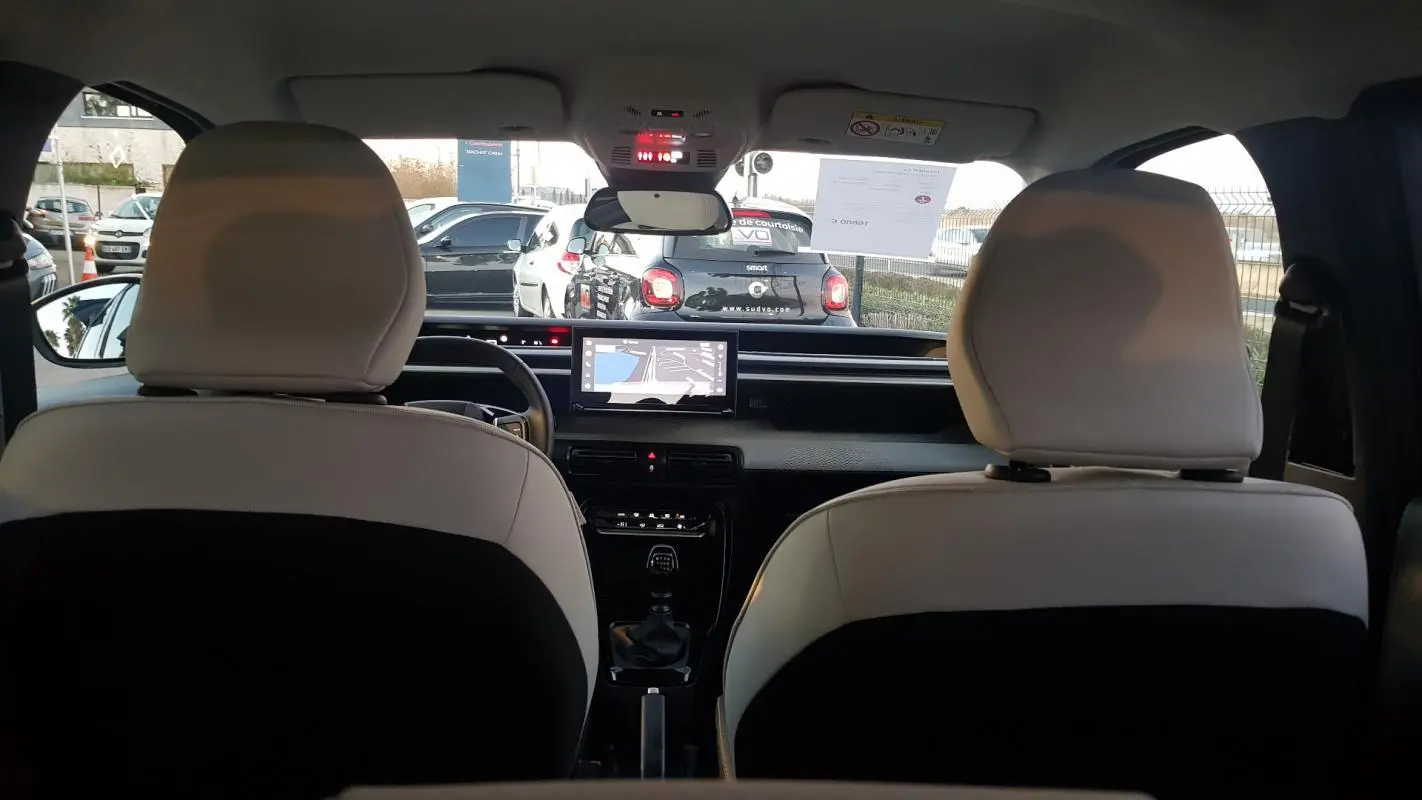 Vue intérieure arrière de la Citroën C3 2025 noire, montrant les sièges bicolores et l'écran tactile central.