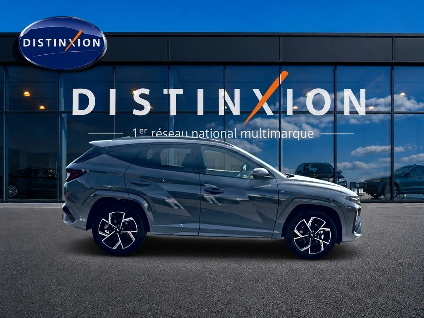Vue latérale droite du Hyundai Tucson 2026 gris shadow avec jantes alu noires et détails N Line devant une vitrine Distinxion.