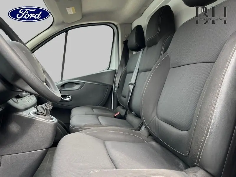 Vue intérieure côté conducteur montrant les sièges tissu Kompo noirs et la console centrale d'un Renault Trafic Fourgon blanc.