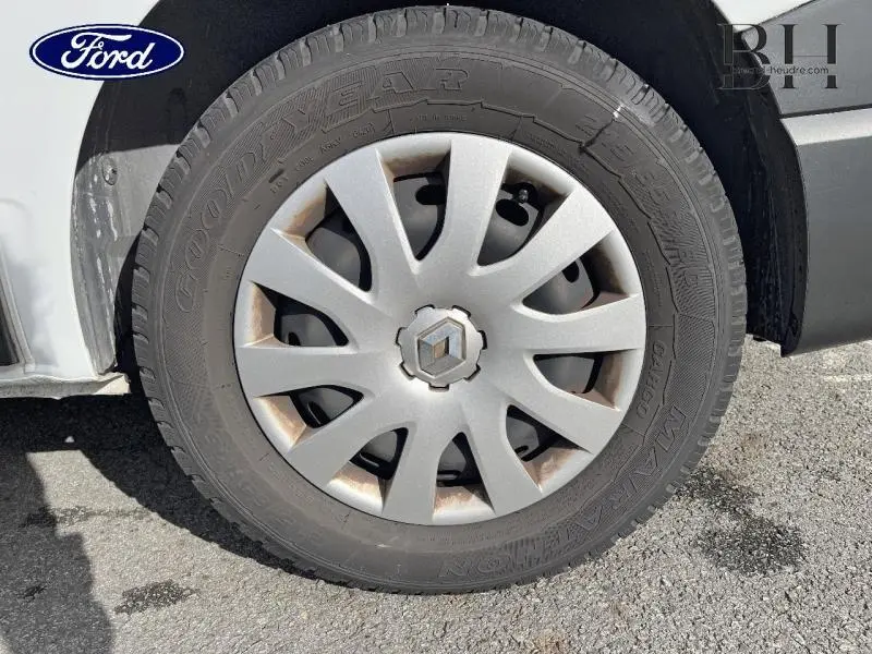 Gros plan sur la roue avant gauche d'un Renault Trafic blanc glacier avec enjoliveur et logo Renault visible.