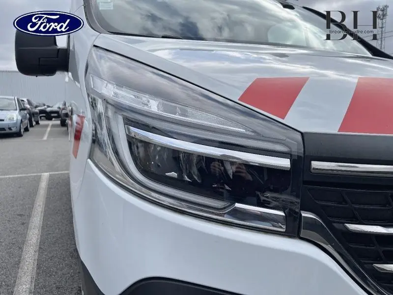 Gros plan sur le phare avant droit du Renault Trafic Fourgon blanc Glacier avec bandes rouges sur le capot.