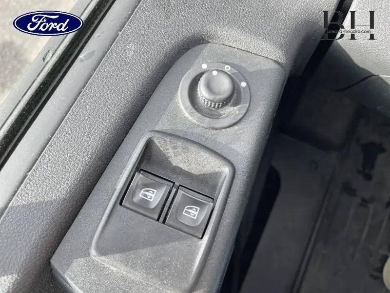 Gros plan sur les commandes de lève-vitres et réglage des rétroviseurs côté conducteur d'un Renault Trafic blanc.