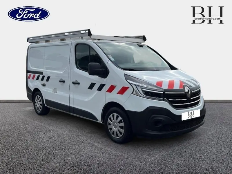 Renault Trafic Fourgon blanc glacier en 3/4 avant droit avec galerie de toit aluminium et marquages rouges et noirs.