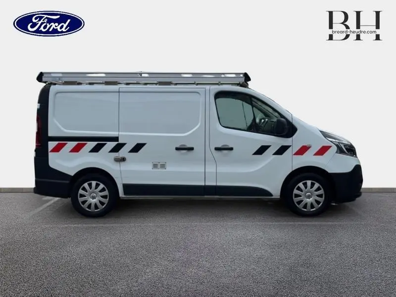 Profil droit d’un Renault Trafic Fourgon blanc glacier avec galerie de toit aluminium et bandes rouges et noires sur la carrosserie.
