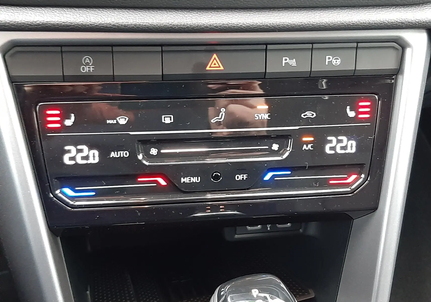Vue rapprochée du tableau de bord et de la console centrale du Volkswagen T-Roc 1.5 TSI gris, avec commandes de climatisation digitales et levier de boîte auto.