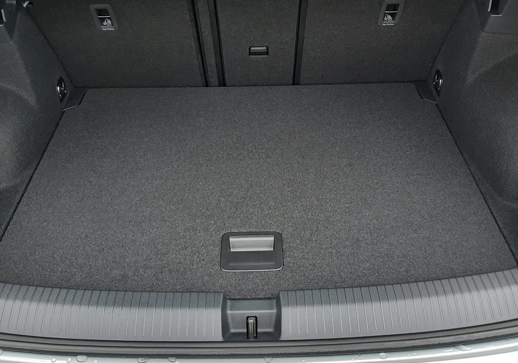 Vue plongeante sur le coffre spacieux et propre du Volkswagen T-Roc 1.5 TSI gris pyrite, avec tapis gris foncé.