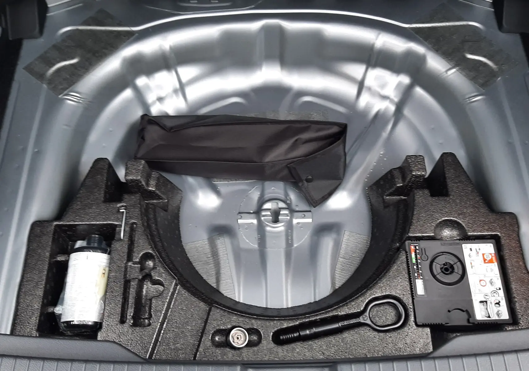 Vue plongeante sur le compartiment de roue de secours gris pyrite d’un Volkswagen T-Roc 2025 avec kit de réparation.