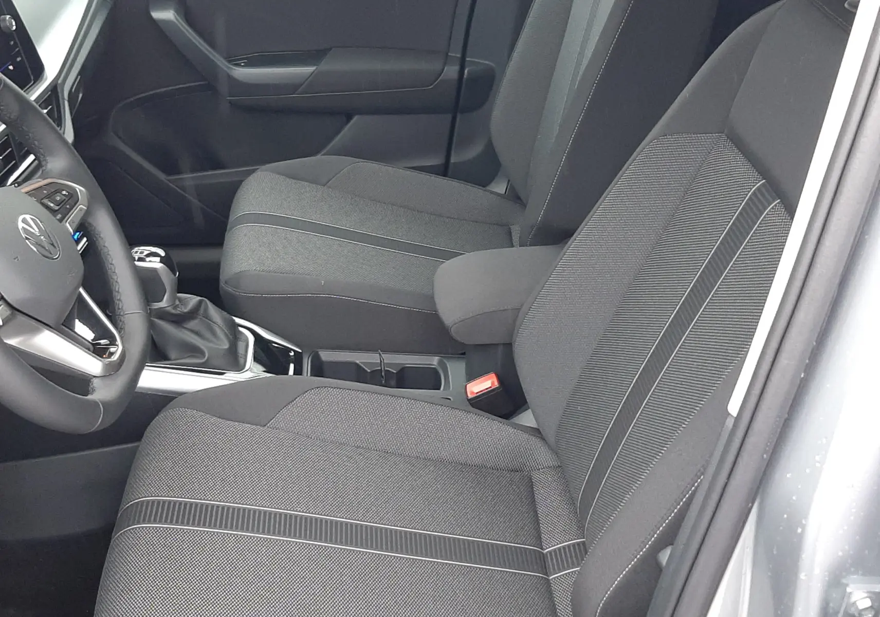 Vue intérieure côté droit du Volkswagen T-Roc 2025 gris pyrite, sièges tissu noir avec surpiqûres grises et console centrale.