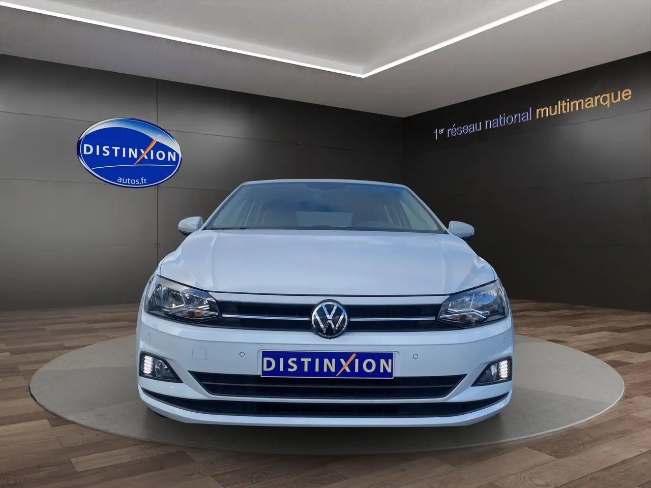 Volkswagen Polo blanc pure vue de face en intérieur, avec phares et feux diurnes allumés.