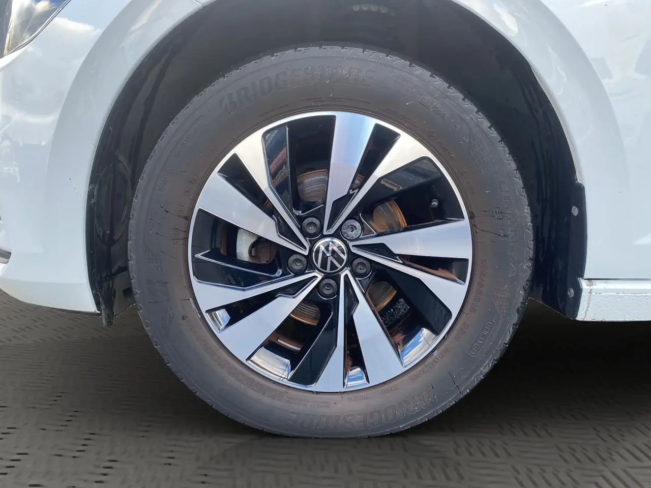 Gros plan sur la roue avant droite d'une Volkswagen Polo blanche avec jante alliage bicolore brillante.