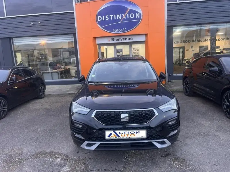 Vue avant d'un SEAT Ateca noir Magique Métal garé devant un concessionnaire avec calandre hexagonale chromée.