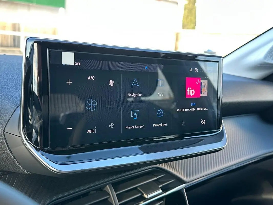 Écran tactile central du tableau de bord de la Peugeot 208 Hybrid blanc, avec commandes climatisation et navigation visibles.