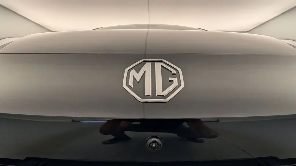 Gros plan sur le logo MG en relief sur la malle arrière Pebble Black, avec caméra de recul visible en dessous.