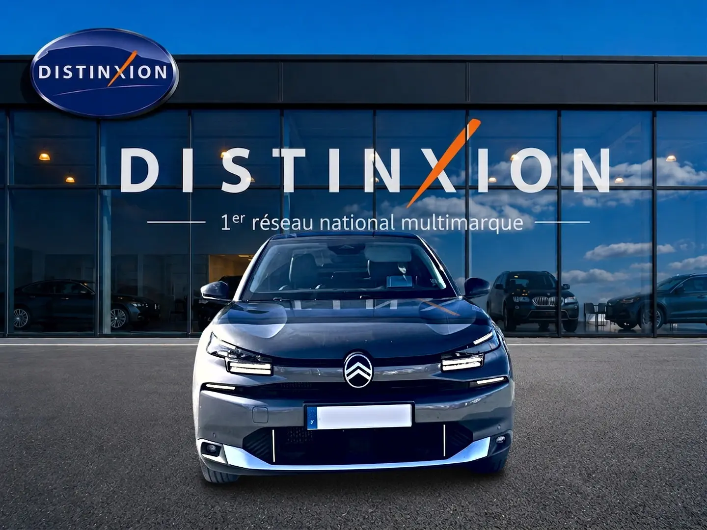Vue frontale d'une Citroën C4 X gris mercure 2025, avec calandre noire et feux LED distinctifs, devant un showroom Distinxion.