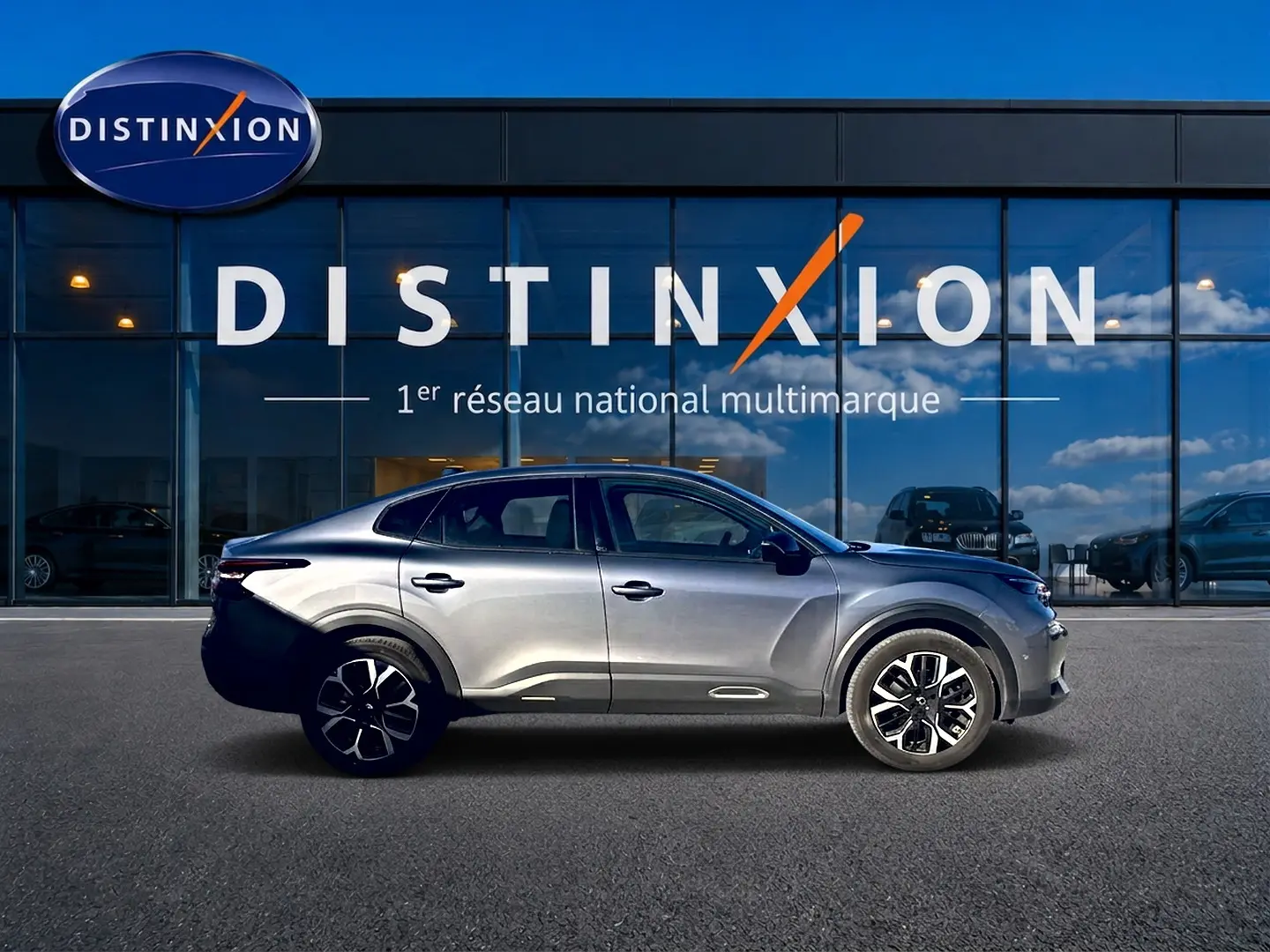 Profil côté gauche d'une Citroën C4 X gris mercure 2025, avec jantes alliage et lignes fluides, devant une vitrine Distinxion.