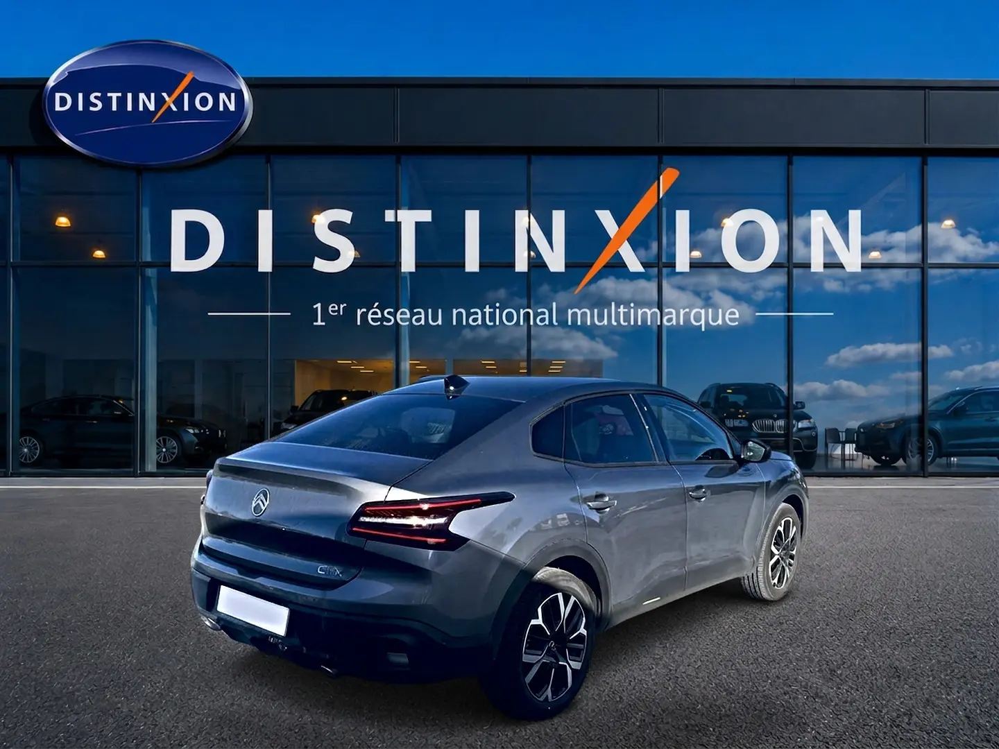 Vue 3/4 arrière droite d'une Citroën C4 X gris mercure avec feux LED et jantes alu devant un showroom Distinxion.