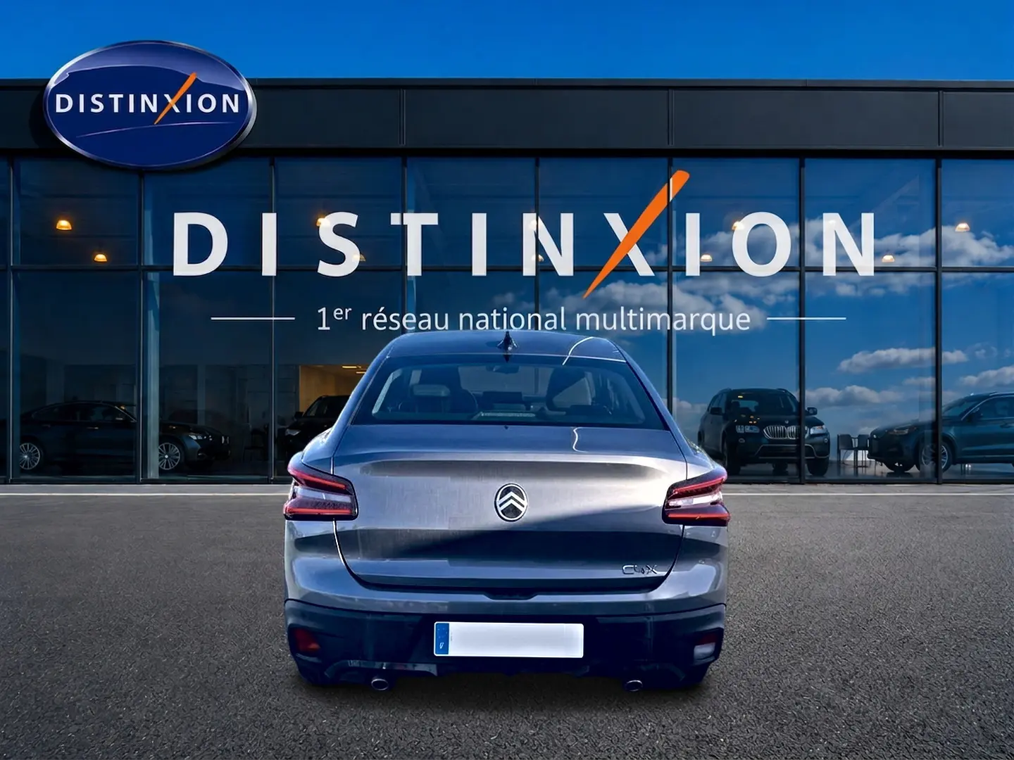 Vue arrière d'une Citroën C4 X gris mercure stationnée devant une vitrine Distinxion avec doubles sorties d'échappement.