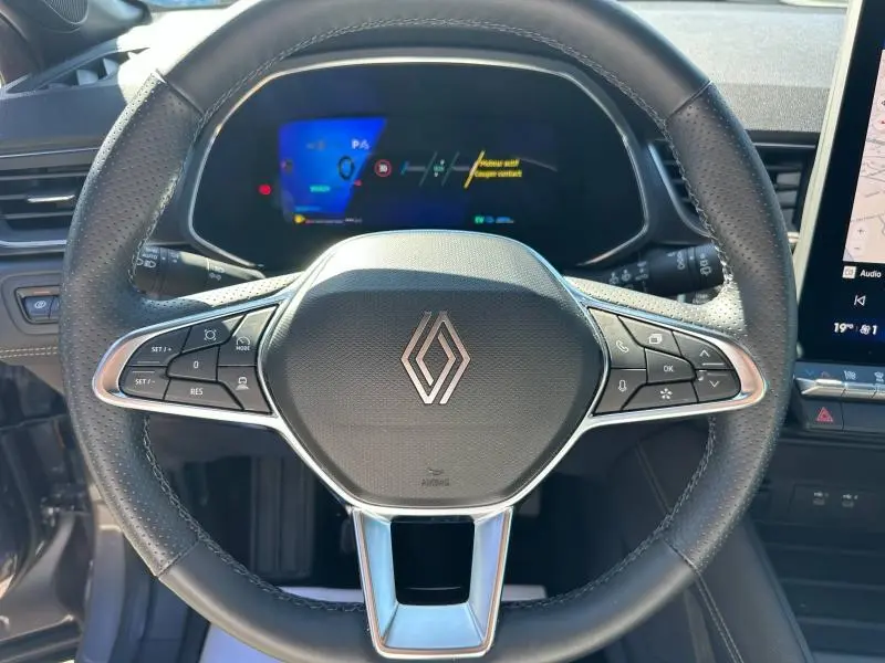 Vue rapprochée du volant multifonction noir avec logo Renault et tableau de bord numérique du Renault Symbioz rouge.