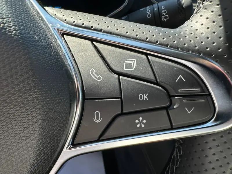 Gros plan sur les commandes multifonctions noires du volant perforé côté droit du Renault Symbioz rouge 2025.