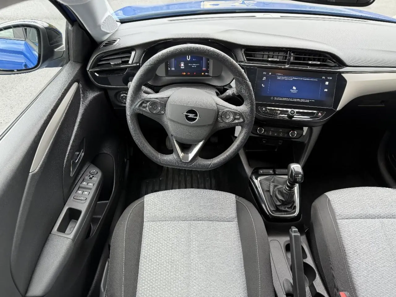 Vue intérieure centrée sur le volant et la console d’une Opel Corsa 2025, boîte manuelle, avec rétroviseur bleu voltaik visible.