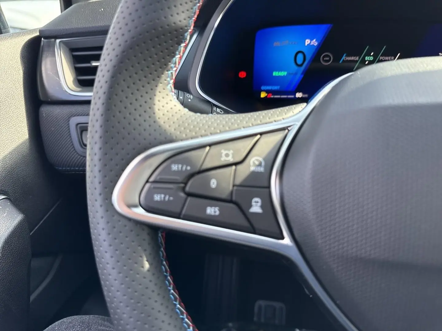 Gros plan sur le volant perforé côté gauche du Renault Symbioz blanc nacré avec commandes multifonctions et tableau de bord digital.