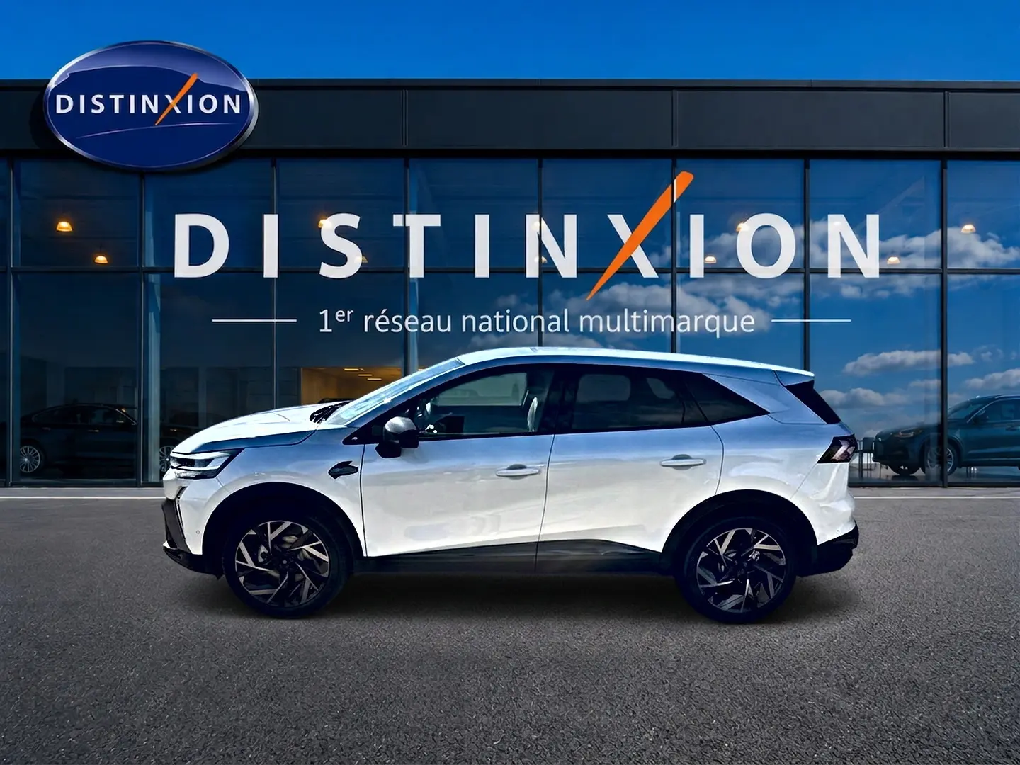 Profil droit du Renault Symbioz blanc nacré 2026 avec jantes alu et toit noir devant un showroom Distinxion.