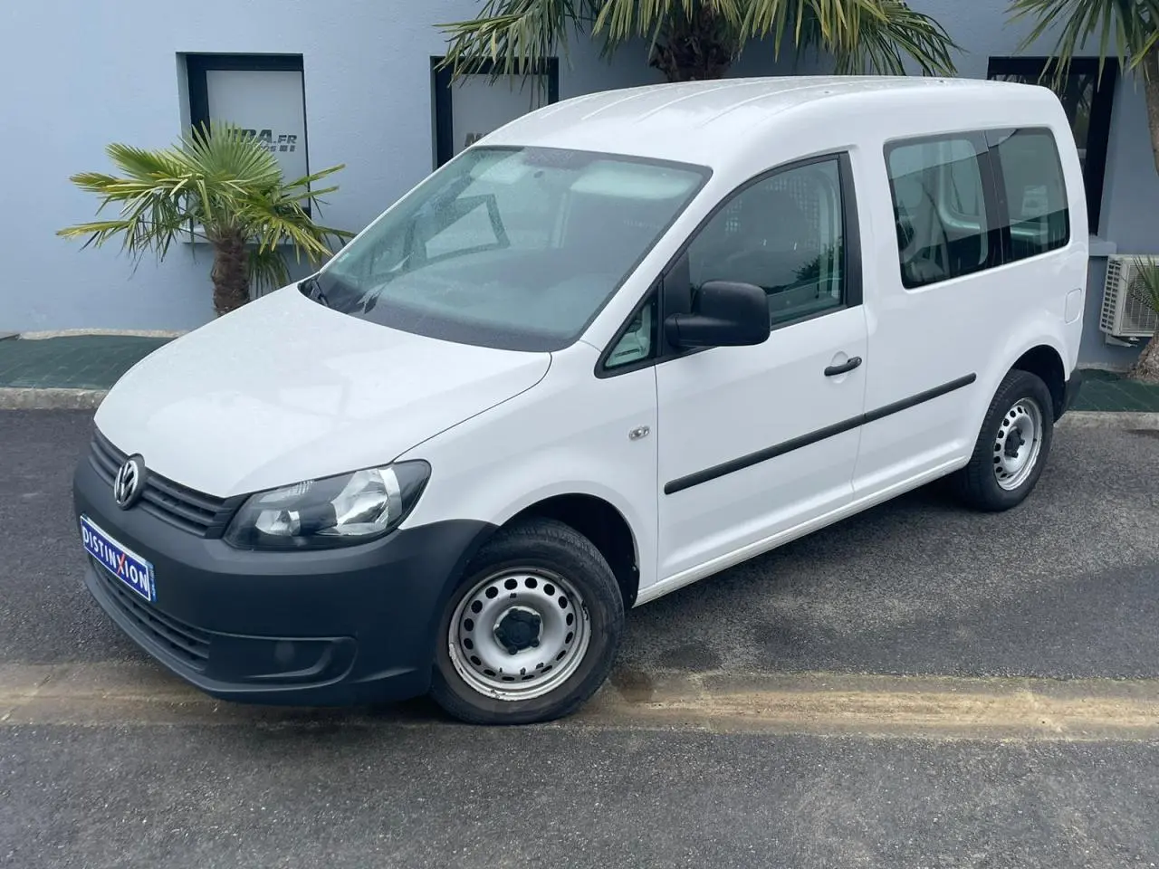 Volkswagen Caddy blanc Candy vu en 3/4 avant droit avec pare-chocs noirs et jantes acier simples.