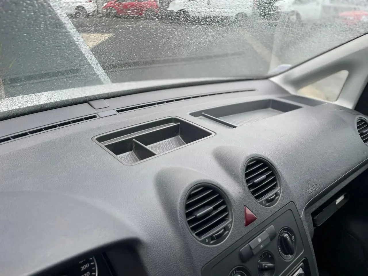 Tableau de bord noir du Volkswagen Caddy 2014 vu de l'intérieur côté passager, avec aérateurs ronds et rangement intégré.