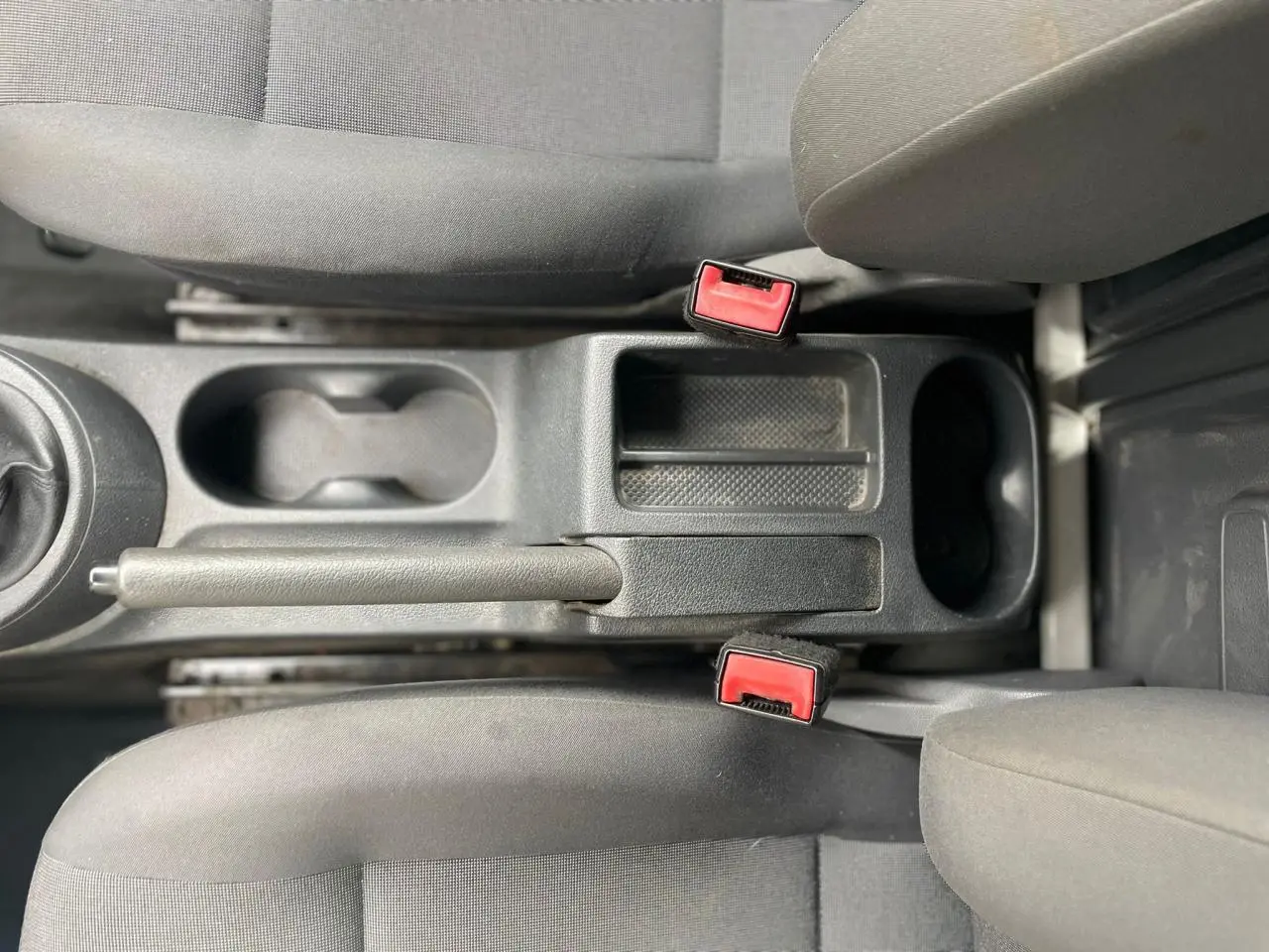 Vue plongeante sur la console centrale et les sièges avant gris du Volkswagen Caddy Van 2014, avec frein à main et ceintures rouges.