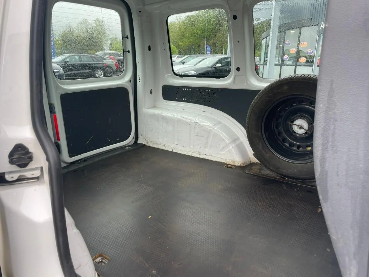 Intérieur du coffre du Volkswagen Caddy blanc Candy 2014, vue arrière droite avec roue de secours visible.