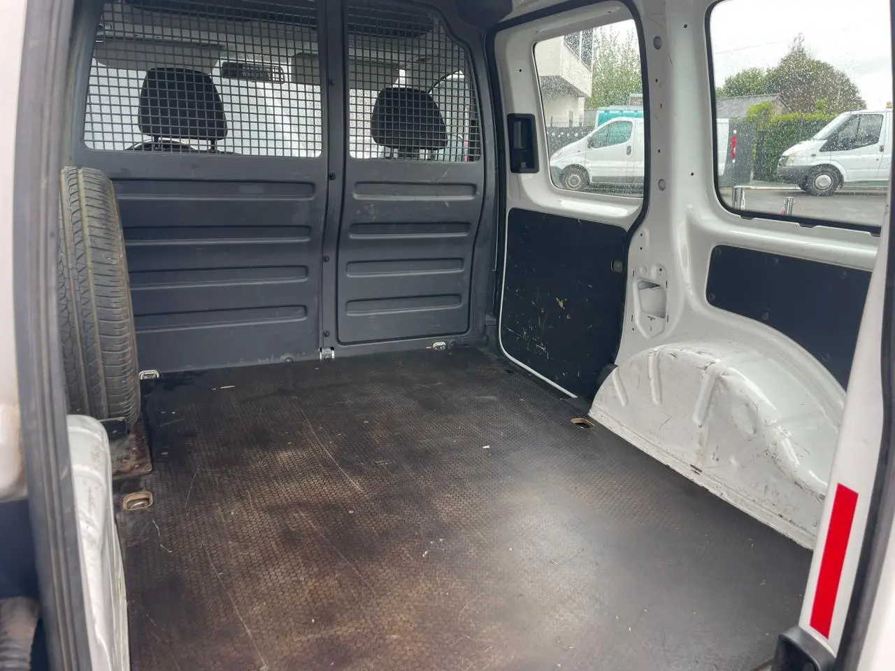 Vue intérieure arrière du Volkswagen Caddy blanc Candy montrant l'espace de chargement avec roue de secours fixée à gauche.