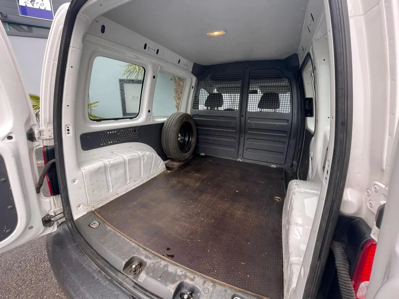 Vue intérieure arrière du Volkswagen Caddy blanc Candy 2014, montrant l'espace de chargement avec roue de secours.