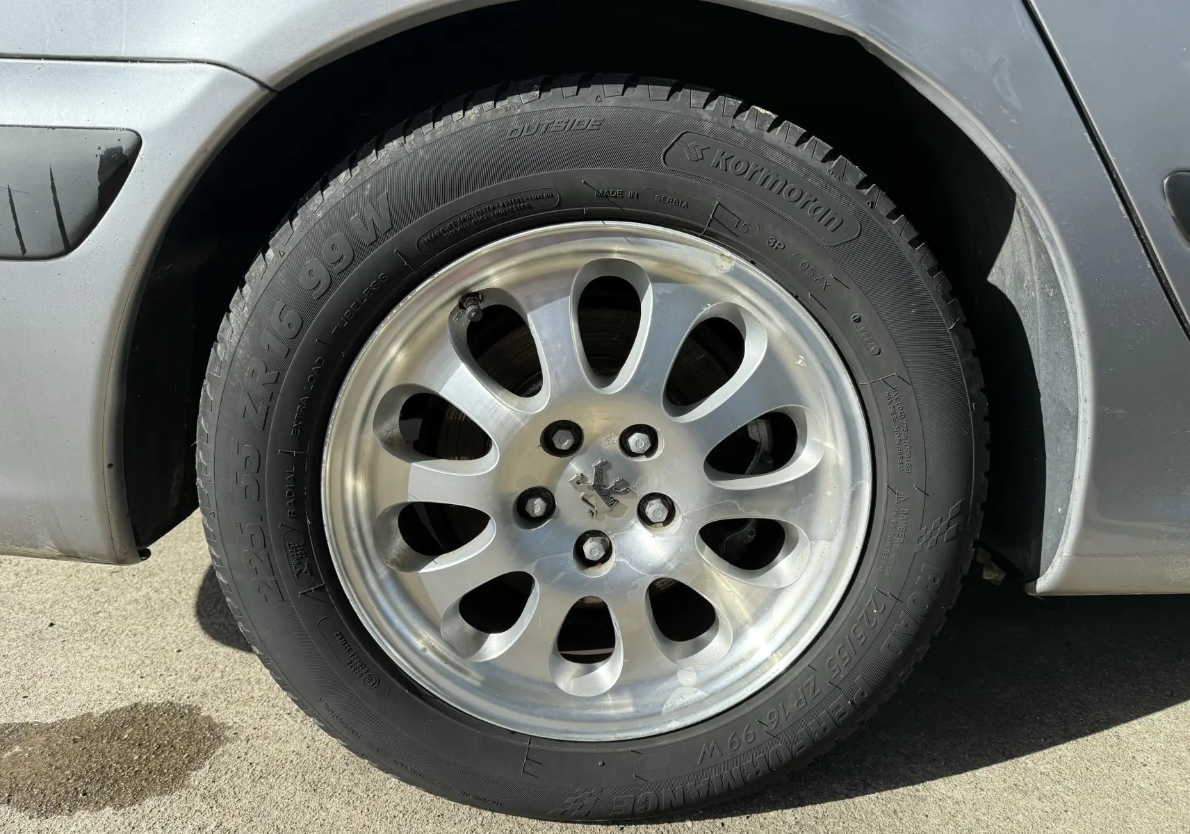 Gros plan sur la roue avant gauche grise d'une Peugeot 607 2.2 i 160 Executive avec jante alu à dix branches.