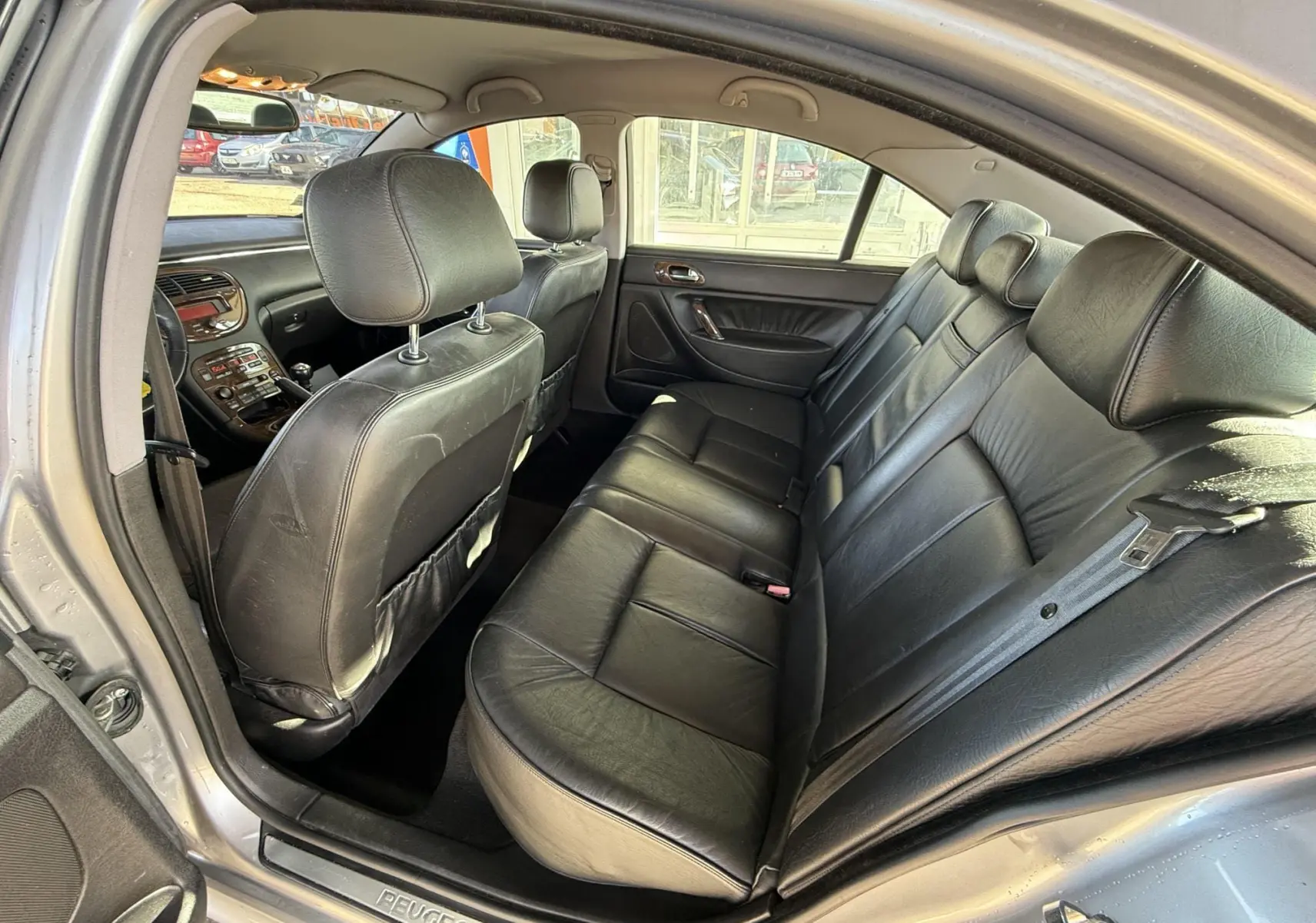 Vue intérieure arrière droite de la Peugeot 607 gris, sièges en cuir noir et tableau de bord visible à l'avant.