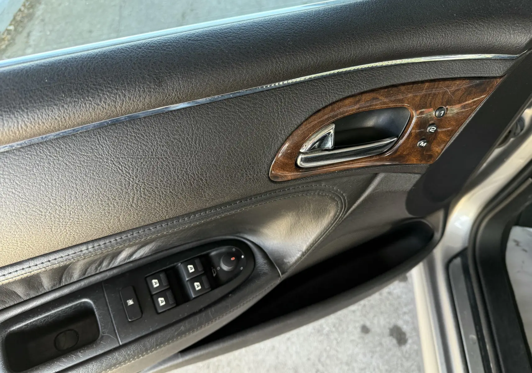 Vue intérieure du panneau de porte avant gauche en cuir noir avec insert bois sur Peugeot 607 gris.