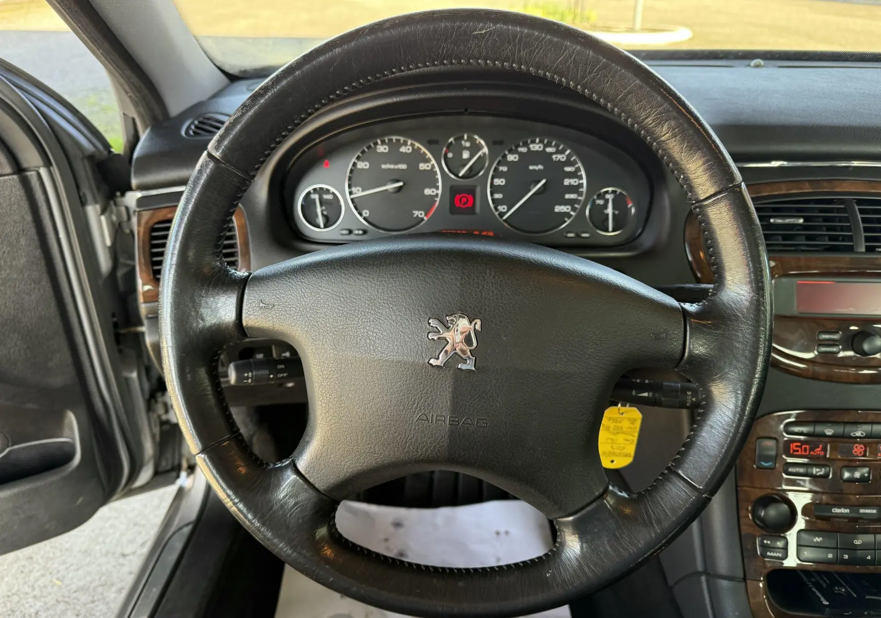 Volant en cuir noir avec logo Peugeot au centre, tableau de bord et console centrale en bois sur Peugeot 607 gris, vue de face intérieure.