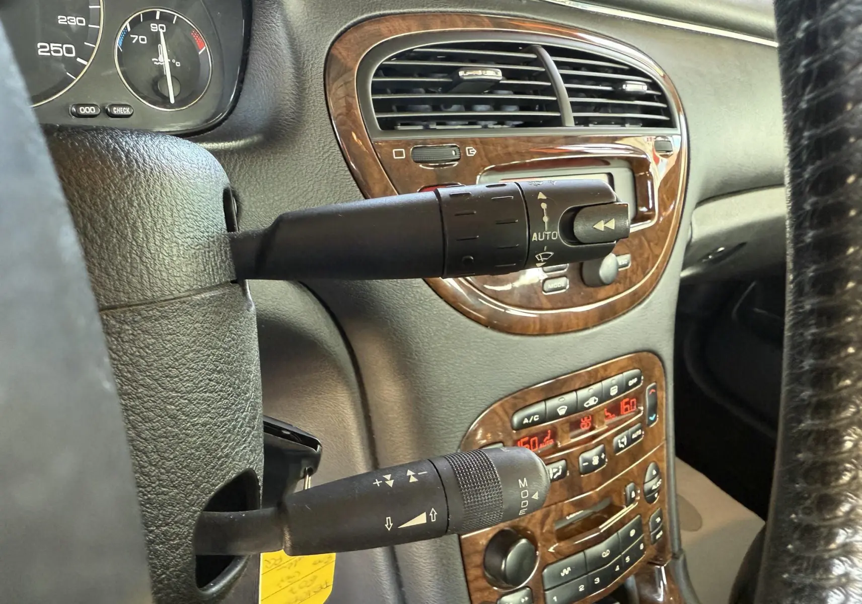 Gros plan sur la console centrale et les commandes de la Peugeot 607 gris, avec finition bois et affichage digital rouge.