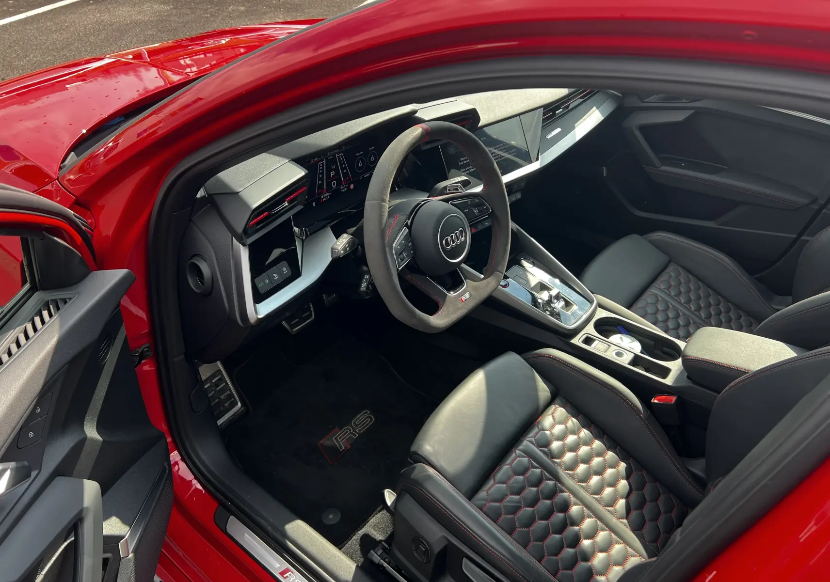 Vue intérieure côté conducteur de l'Audi RS3 Sportback rouge 2022, sièges cuir noir à surpiqûres rouges et volant sport.