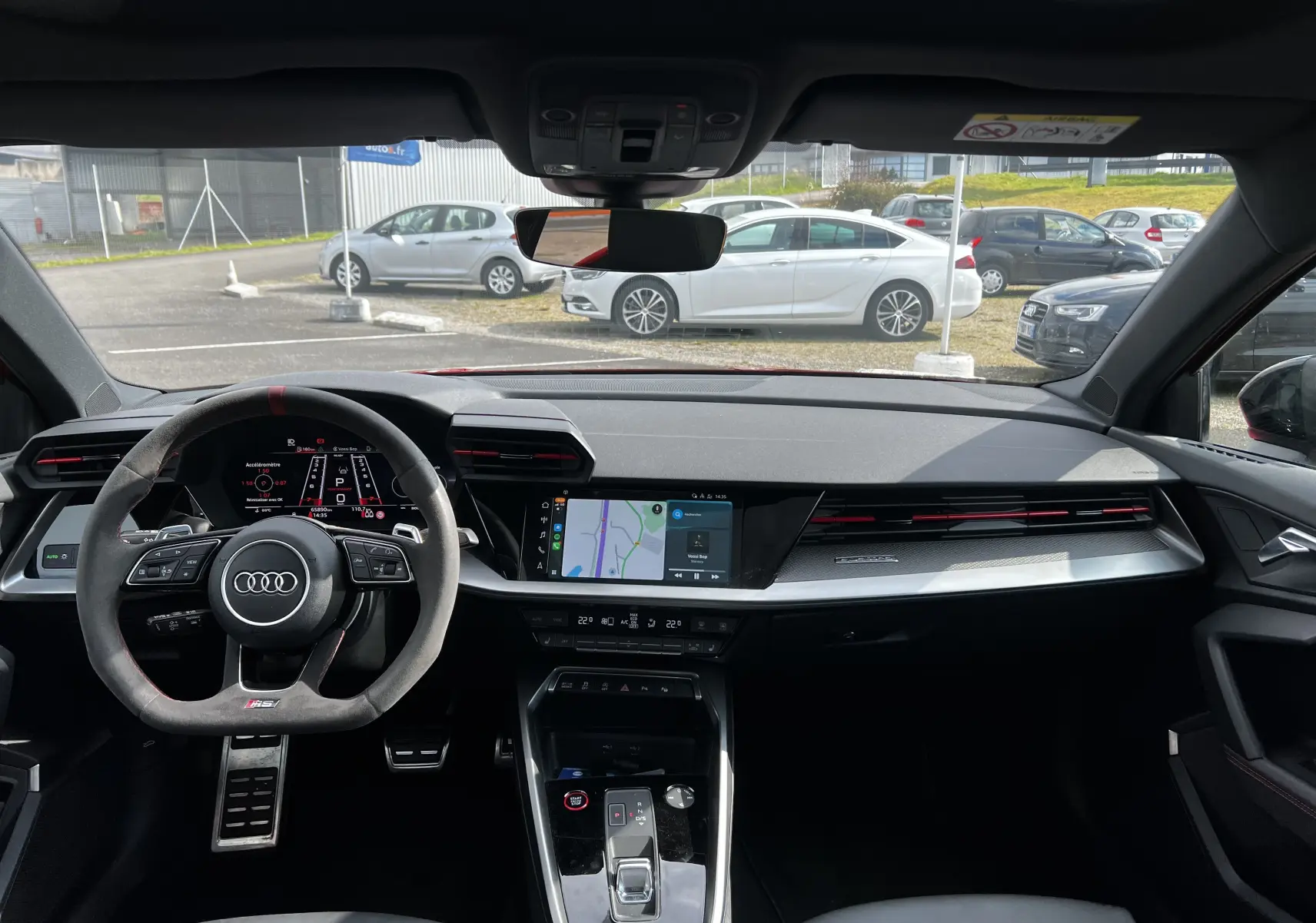 Vue intérieure de l'Audi RS3 Sportback 2022 avec tableau de bord noir, volant sport et écran tactile central affichant la navigation.