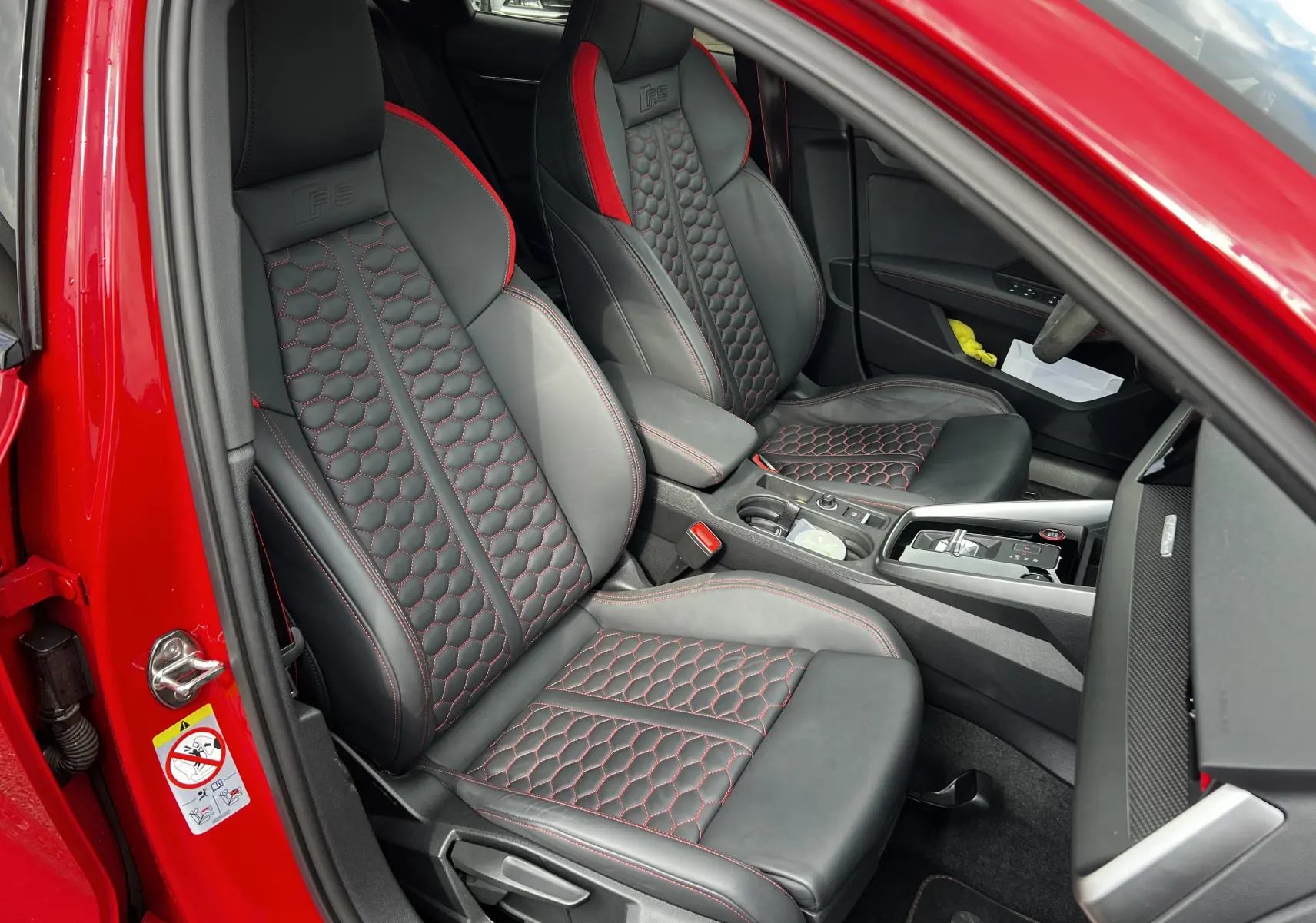 Intérieur d'Audi RS3 Sportback rouge 2022, sièges sport noirs avec surpiqûres rouges et logo RS embossé.