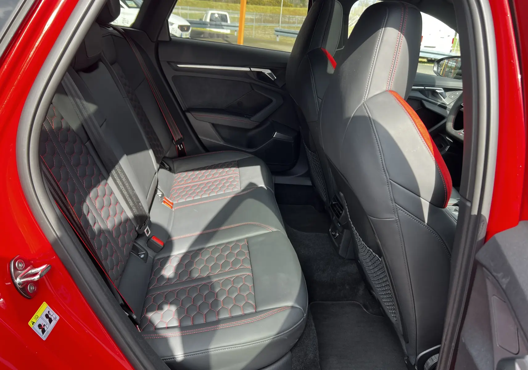 Vue intérieure côté gauche arrière de l'Audi RS3 Sportback rouge 2022 avec sièges en cuir noir à surpiqûres rouges.