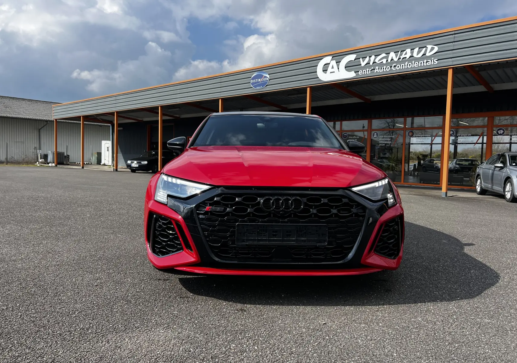 Vue de face d'une Audi RS3 Sportback rouge 2022 avec calandre noire et phares LED distinctifs.