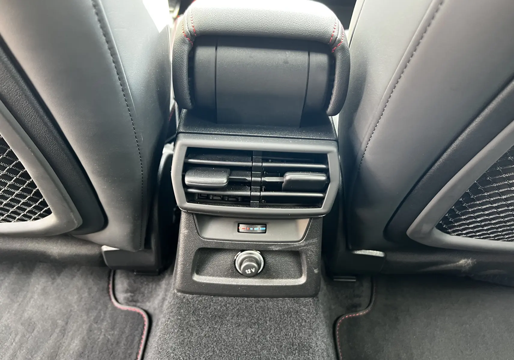 Vue rapprochée des aérateurs arrière et prise 12V entre les sièges noirs de l'Audi RS3 Sportback rouge 2022.