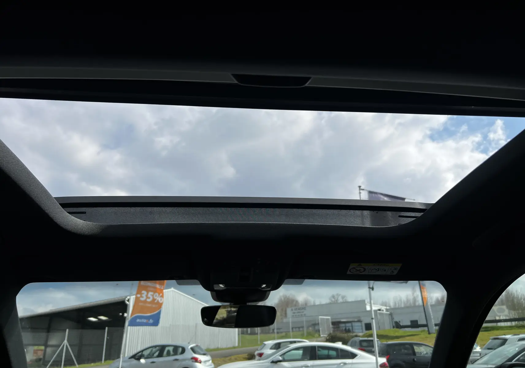 Vue intérieure du toit ouvrant panoramique de l'Audi RS3 Sportback rouge 2022, avec ciel nuageux visible.
