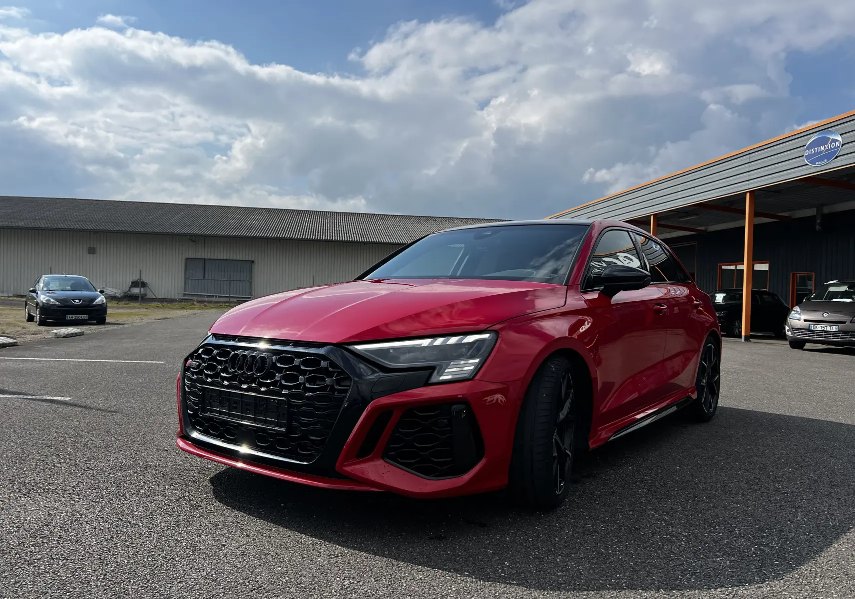 Audi RS3 Sportback rouge vue 3/4 avant droit, calandre noire et jantes noires, stationnée en extérieur.