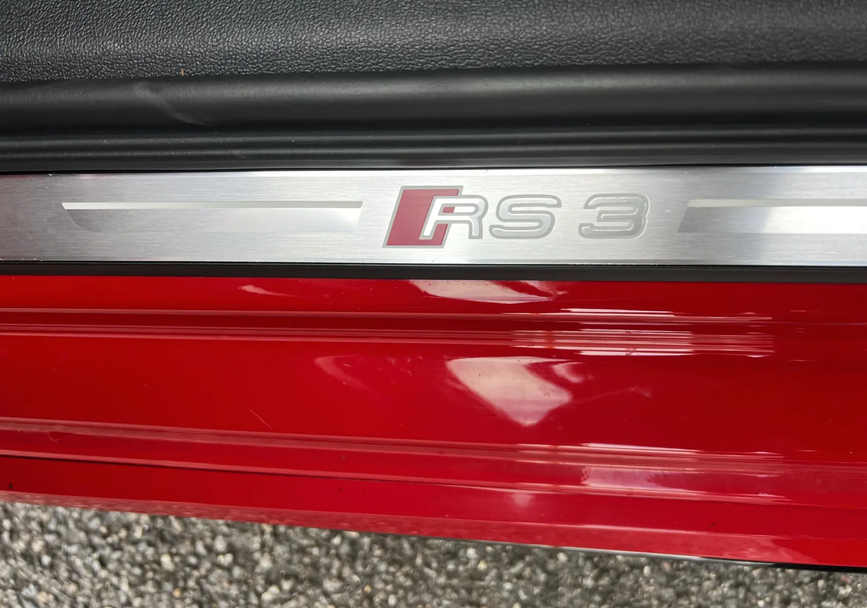 Gros plan sur la plaque de seuil de porte rouge d'une Audi RS3 Sportback avec logo RS3 en métal brossé.